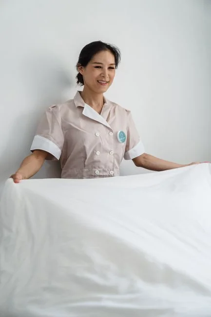 a-woman-in-a-green-shirt-and-black-gloves-vacuuming-a-gray-ottoman-5txz228u4eo